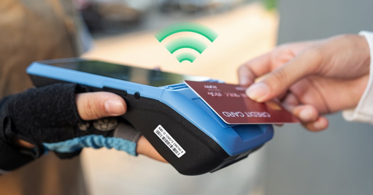 Image of an IoT Point of Sale (POS) device with a small screen, numeric keypad, and card reader slot. The device displays a digital interface for processing payments. A label on the back of the device shows an IMEI number, used for device identification, printed in black text on a white background